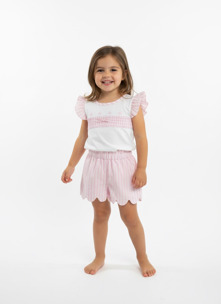 Young girl wearing a white top with pink accents and pink shorts on a white background