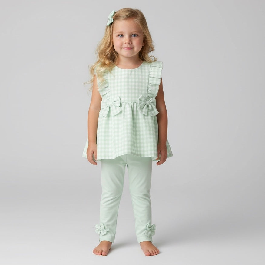 Young girl wearing a light green checkered outfit with ruffles on a plain background