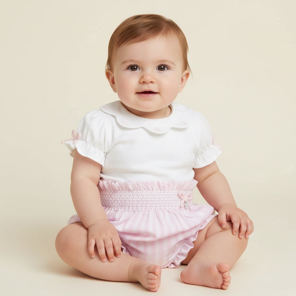 Baby wearing a white top and pink bloomers sitting on a beige background