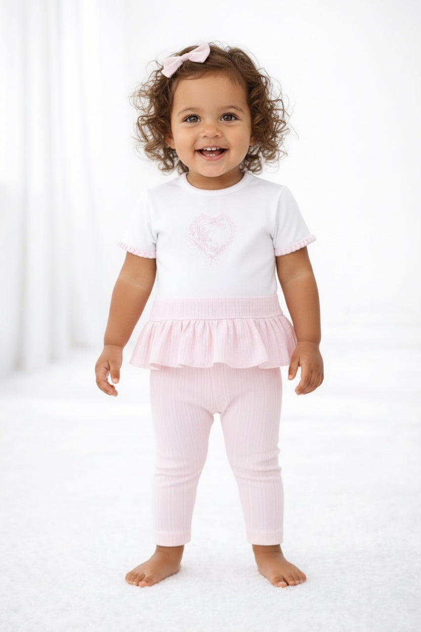 Child wearing a white top with a pink ruffled layer and matching pants on a white background