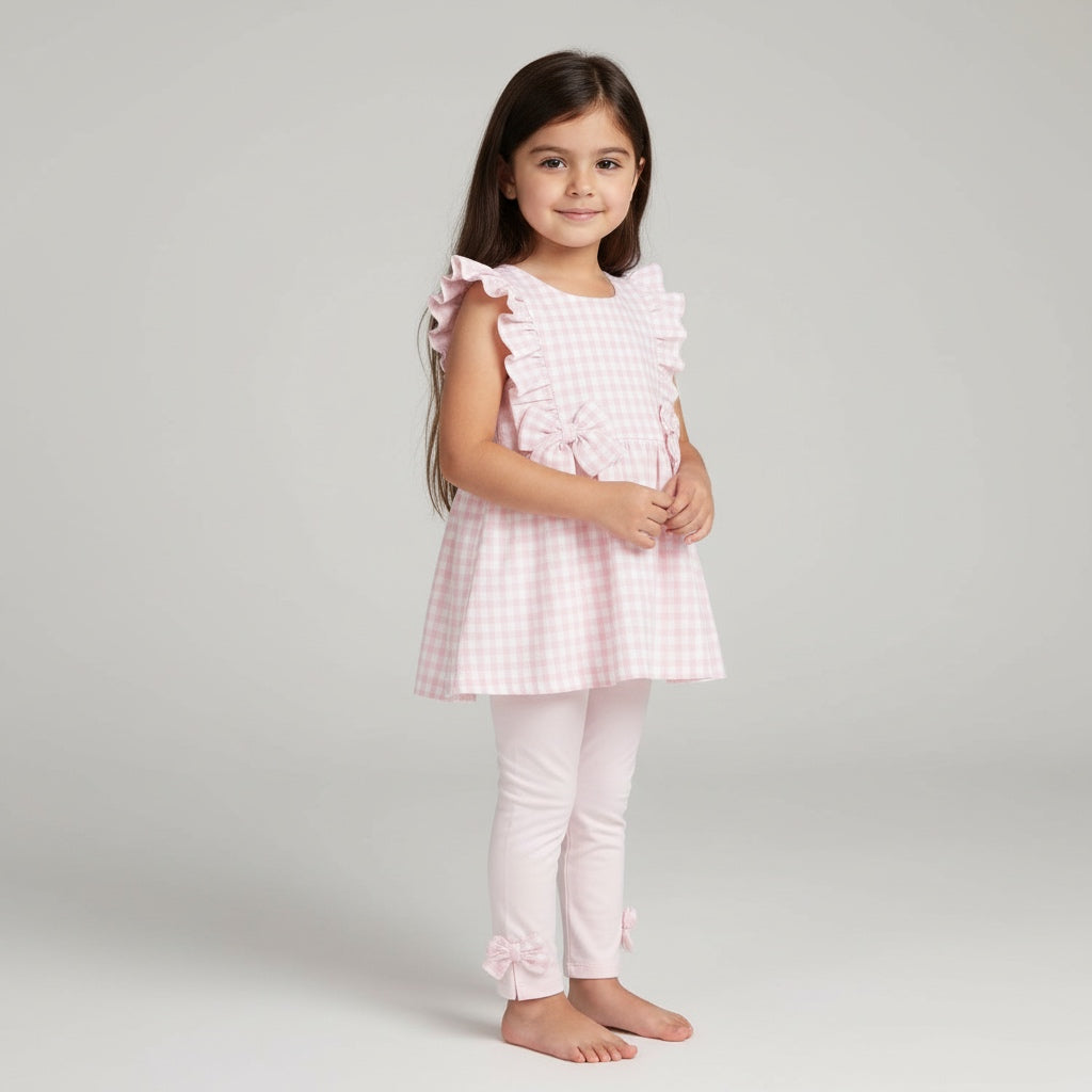 Young girl wearing a pink checkered outfit with ruffled sleeves on a light gray background