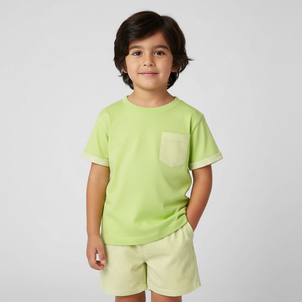 Child wearing a light green t-shirt with a pocket and light-colored shorts on a plain background